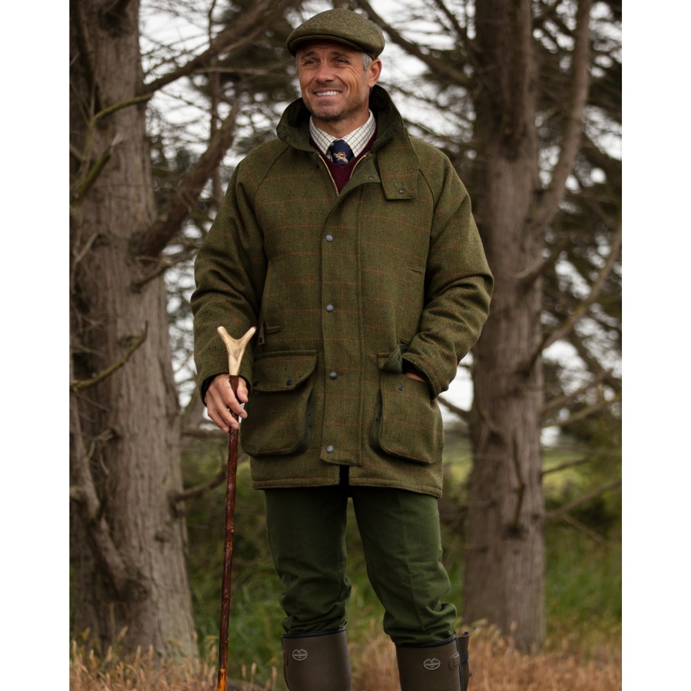 Male model stood in the woods wearing a Walker & Hawkes Barlaston tweed jacket in dark sage.