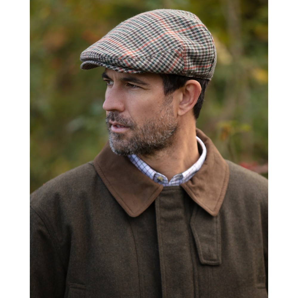 Male model wearing a Walker & Hawkes Braxton flat cap in cream.