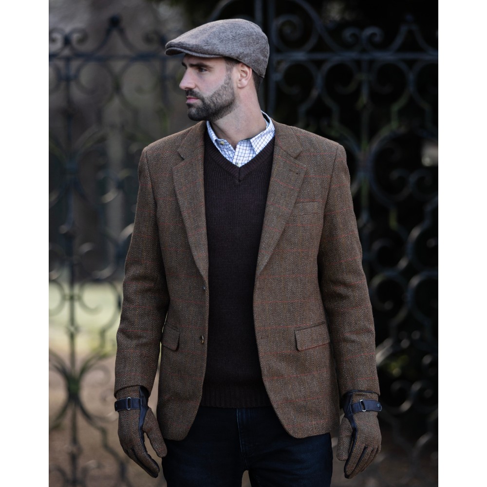 Male model wearing a brown Walker & Hawkes Men's Derby Tweed Windsor Blazer while stood in front of some iron gates.