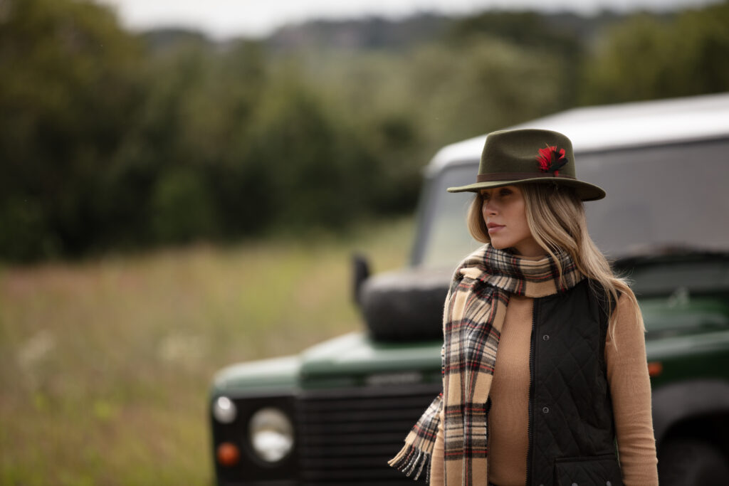 Woman wearing a green felt hat in front of a Land Rover.
