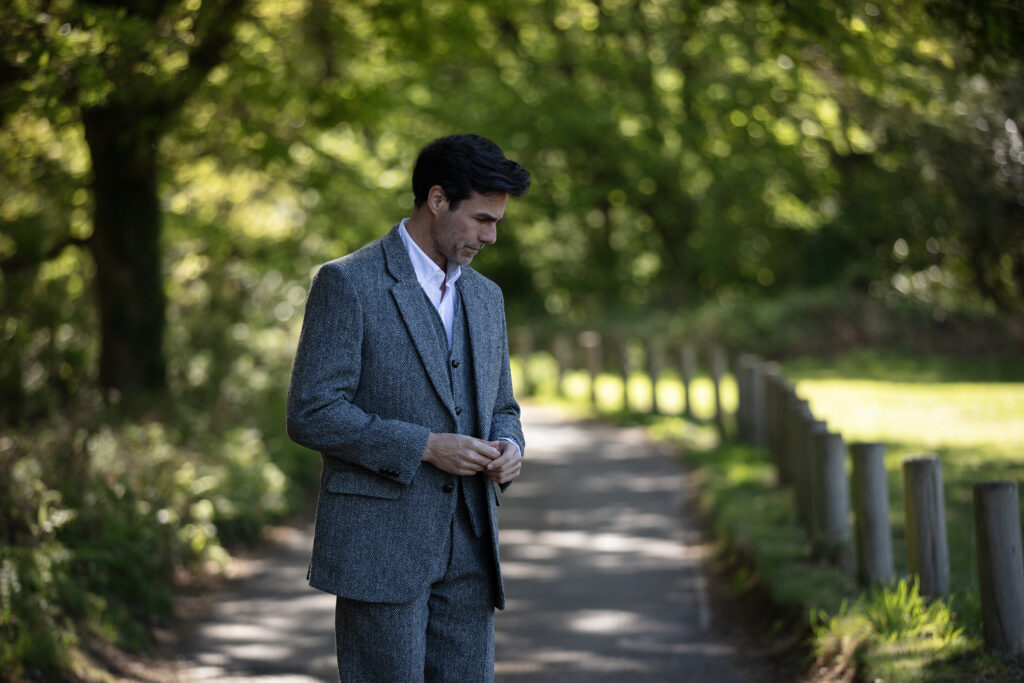 Man wearing a tweed blaze and waistcoat from Walker & Hawkes. with the sun dappling through the trees.