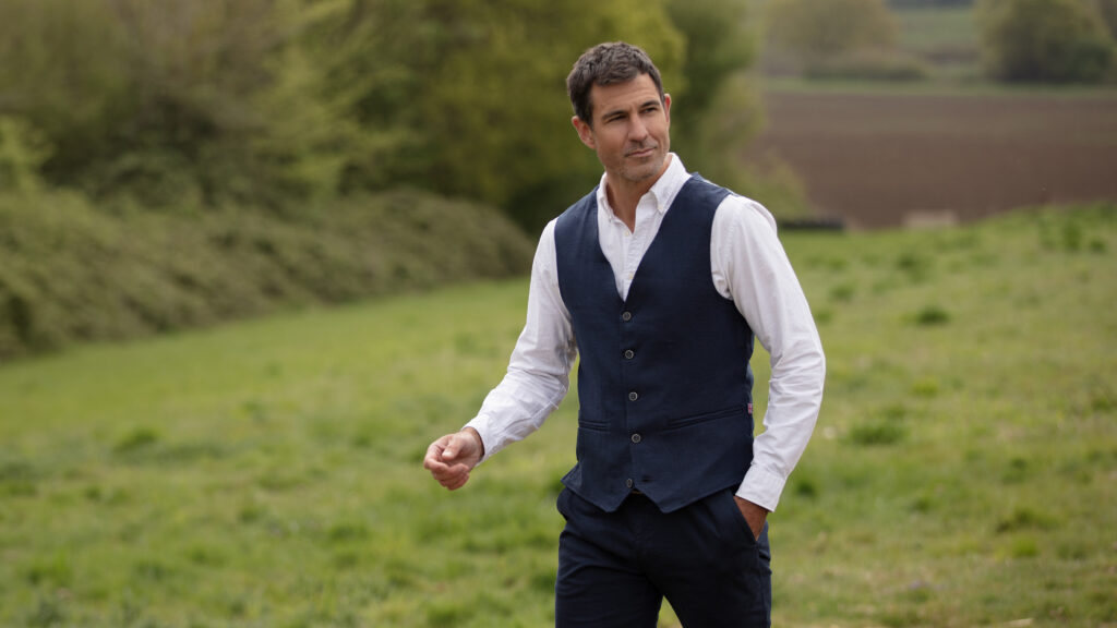 Man stood in a field wearing a Walker & Hawkes Corbet waistcoat.