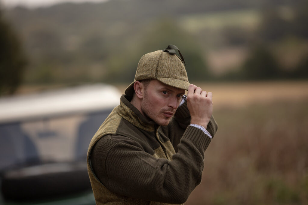 Man pulling on a Walker & Hawkes deerstalker to compliment his shooting jacket.