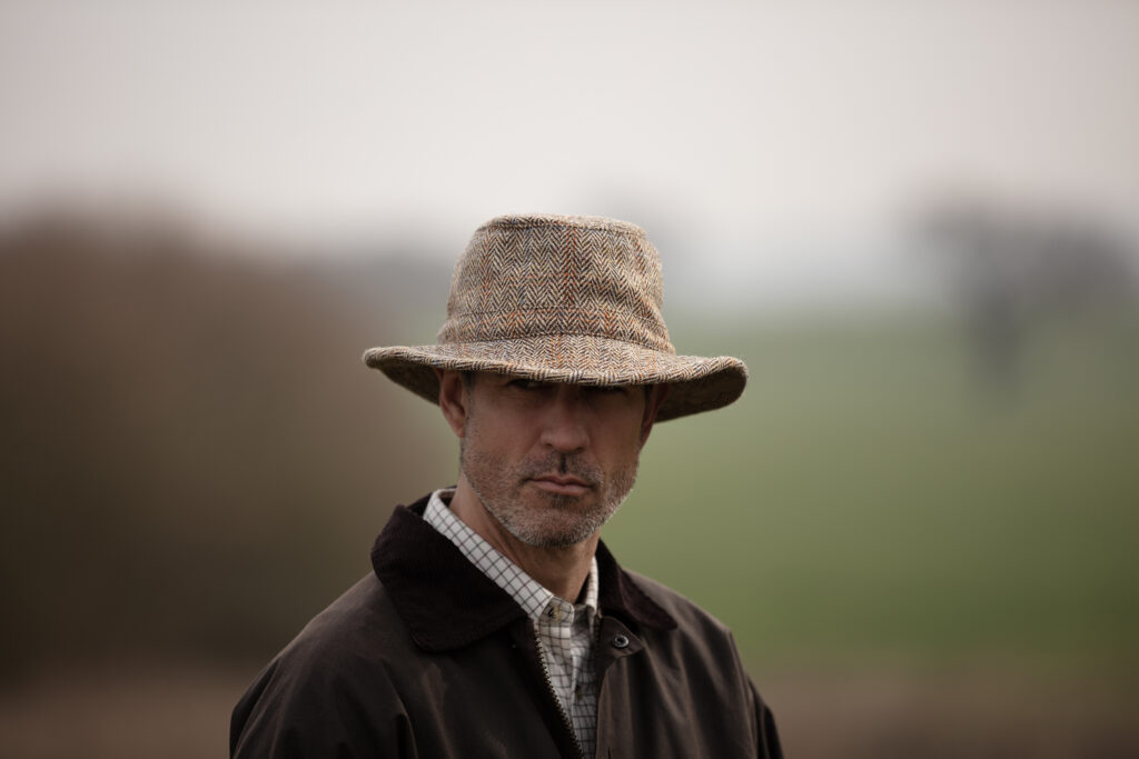 Man dressed for changeable weather with a wax jacket and brimmed hat from Walker & Hawkes.