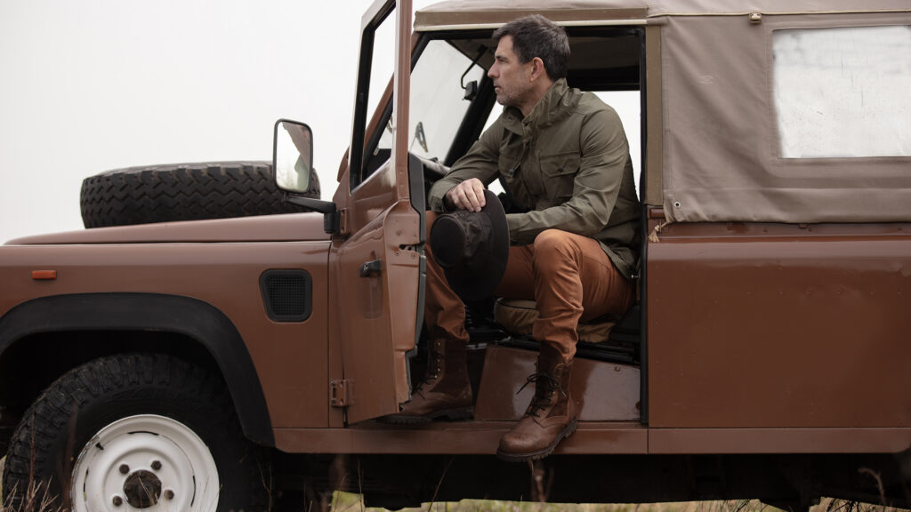 Man sitting in the passender seat of a Land Rover wearing a Walker & Hawkes jacket.